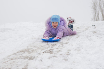 Fototapeta na wymiar Girl rolls down on his stomach with a headfirst slide snow