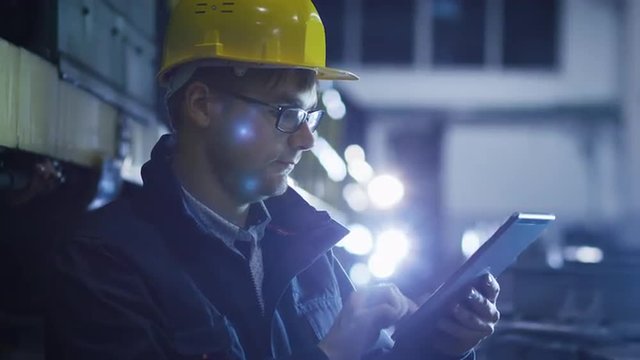 Technician in Glasses and Hard Hat Using Tablet in Industrial Environment. Shot on RED Cinema Camera.
