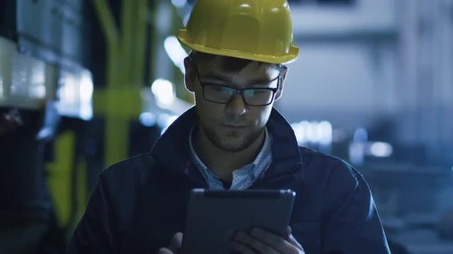 Technician in Glasses and Hard Hat Using Tablet in Industrial Environment. Shot on RED Cinema Camera.