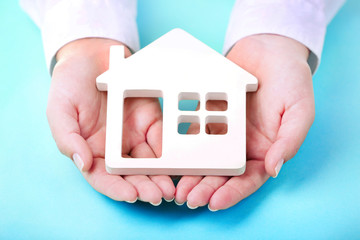 Female hands holding house on turquoise background