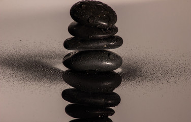 Fototapeta na wymiar Steinmännchen mit schwarzen Steinen Symbol der Gesundheit mit einer Blume
