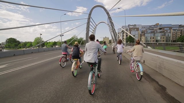 Back side of cycling group of people across bridge in summer cloudness day. 