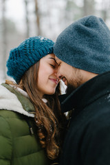 Cute young hipster couple having fun in winter park warming eachother on a bright day hugging each other and smiling 
