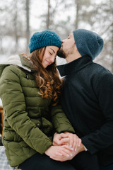 Cute young hipster couple having fun in winter park warming eachother on a bright day hugging each other and smiling 
