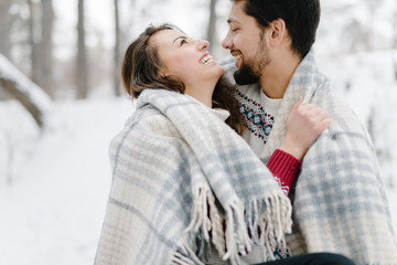 Fototapeta premium Cute young hipster couple having fun in winter park warming eachother on a bright day hugging each other and smiling 
