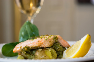 Salmon fillet, pesto and crushed potato plate with wine. A restaurant prepared fish dish presented on a white plate
