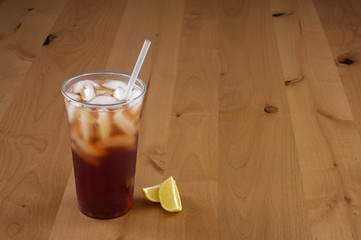 Large fresh brewed Iced tea in a clear cup with a straw and two lemon wedges.