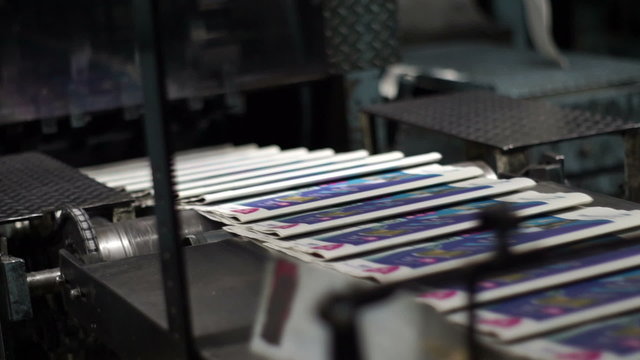 Handheld shot of finished newspapers coming off the printing production line from an industrial offset press printing machine.