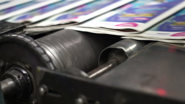 Close up handheld shot of finished newspapers coming off the printing production line from an industrial offset press printing machine.