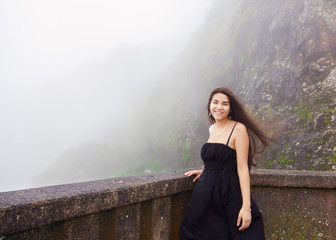 Teen girl standing on foggy hillside in black dress,  smiling