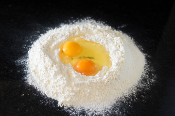 Two eggs in a well in the sifted flour on black countertop