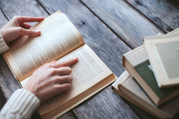 Naklejka premium female hands holding a book and read on wooden desk with books