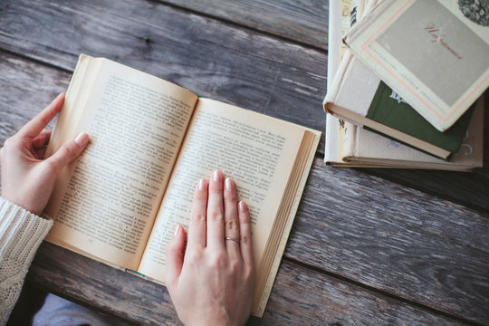 female hands holding a book and read on wooden desk with books