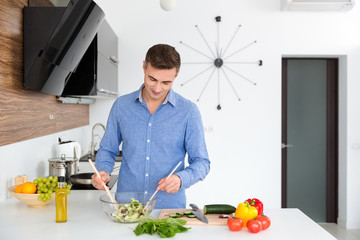 Handsome man in blue shirt mixing vegetables for salad