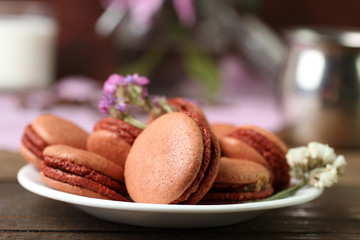 macaroons on a plate with flowers on wooden table. Flowers with glass of milk on a napkin in the background.