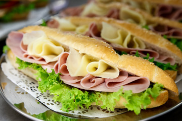 Yellow sliced cheese, ham and salad white  baguettes on doily and stainless steel tray.