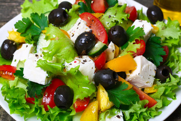 Greek salad with fresh vegetables, feta cheese and black olives on a wooden background