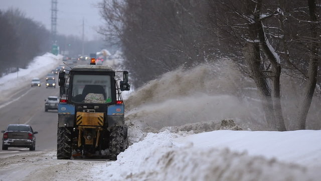Tractors of road service clean up the snow from the roadside and throw it away
