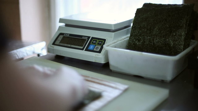 A sushi chef prepares rolls, weighs on the scales a portion of rice and lays out the rice on a sheet of Nori seaweed
