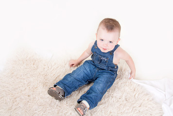 Cute baby with big blue eyes in denim overalls sitting isolated on white background.