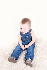 Naklejka premium Cute baby with big blue eyes in denim overalls sitting isolated on white background.