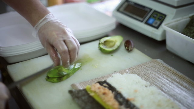 The chef slices the knife avocado for making rolls
