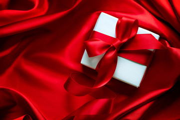 Valentine gift box with red satin ribbon on red silk background
