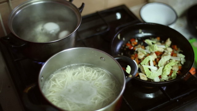 On the gas stove  prepares food, boiled eggs, noodles and fried vegetables
