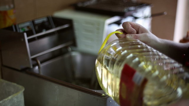 The chef pouring cooking oil into the fryer from a five-liter bottle
