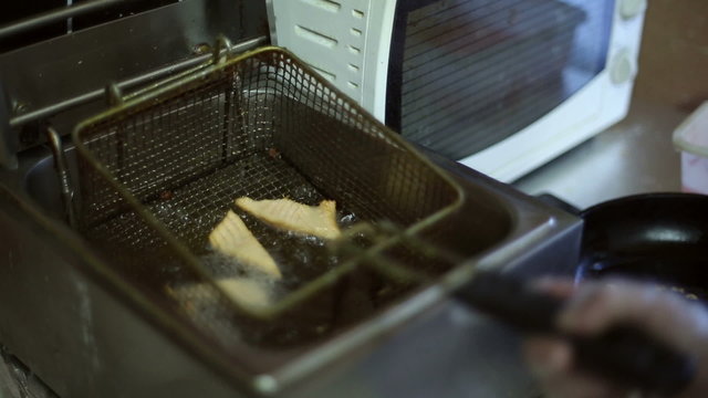 Red fish is fried in a deep fryer, chef raises and lowers the fish into the oil
