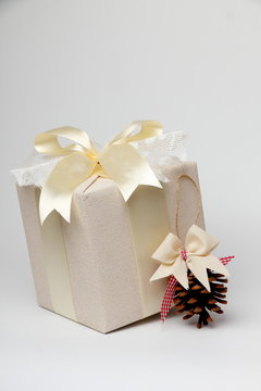 Beautifully wrapped gift with a pine cone./Beautiful gift box with packing beige paper, gold ribbon and lace. Pine cone.