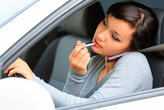 Female driver talking by mobile telephone and doing make-up.