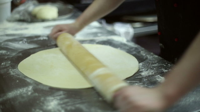 The chef rolls out the dough with a rolling pin, he cooks pizza
