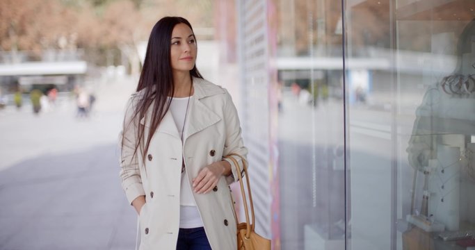 Smiling Stylish Woman Walking Past A Shop Window With A Smile As She Walks Down An Urban Street Towards The Camera