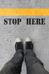 Black shoes standing behind the yellow line and start here sign