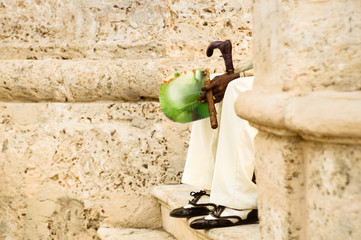Detail of unrecognizable person with cuban cigar sitting on stairs at Havana old city in Cuba - Indigenous man wearing traditional clothing and accessories  - Warm color tones with focus on hands