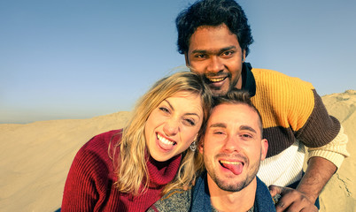 Group of multiracial best friends having fun taking selfie with smartphone on the desert dunes - Young cheerful travelers guys smiling on sunny vacation day - Concept of happiness and friendship 