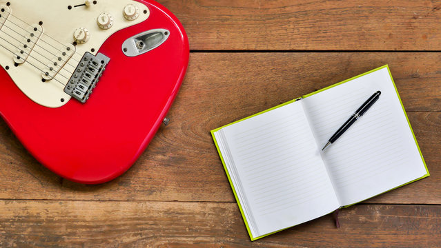 Top view workspace with blank notebook,pen and Electric guitar on wooden table background .