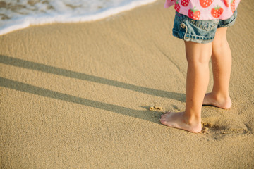 Fototapeta na wymiar Feet of little girl standing alone on the sand beach
