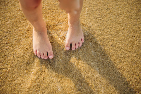 Feet of little girl standing alone on the sand beach