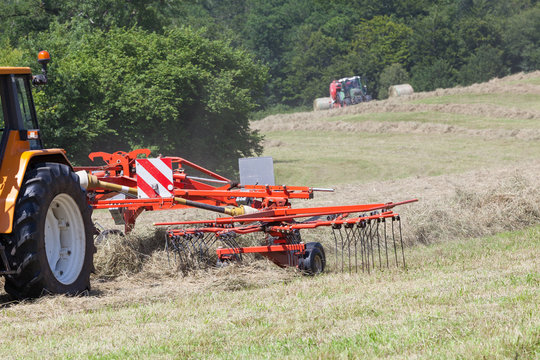 Farmer using a rotary rake to turn drying grass for hay and fodder for livestock, Close up on the hay rake with some motion blur on the tines