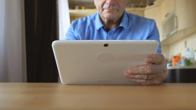 DOLLY: An aged male hands types on a white tablet PC on a table at home
