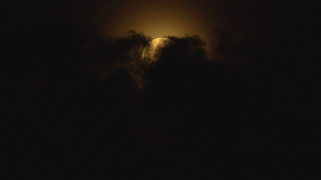 CLOSEUP: A dark clouds covers a full round moon on night sky
