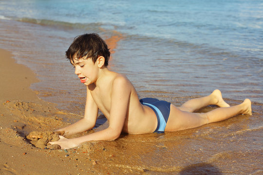 boy on the beach take sun bathing play with sand