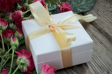 Pink roses and gift box over wooden table, holiday background