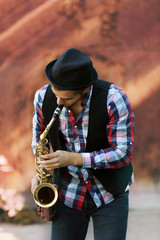 Young man playing on saxophone outside near the old wall