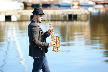 Young man playing on saxophone on the riverside