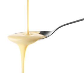 Condensed milk pouring from a spoon, isolated on white