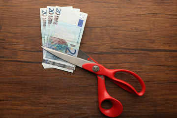 Red scissors cut money on wooden background. Financial concept