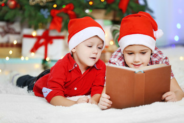 Two cute small brothers reading book on Christmas decoration background